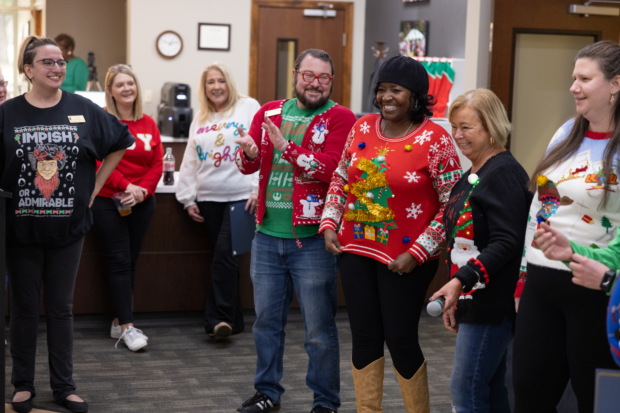 JSCC Employees line up as part of a holiday ugly sweater contest to determine a winner. Many are laughing.